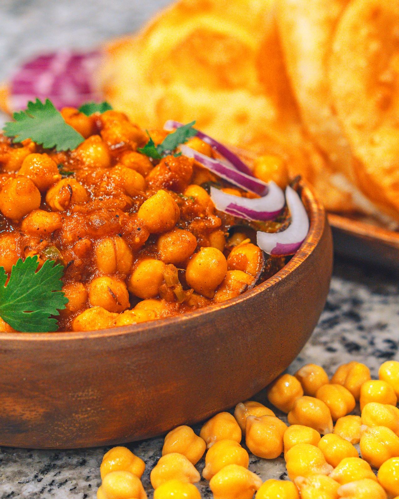 Chole in a wooden bowl with puffed bhature, sliced onion and chilli