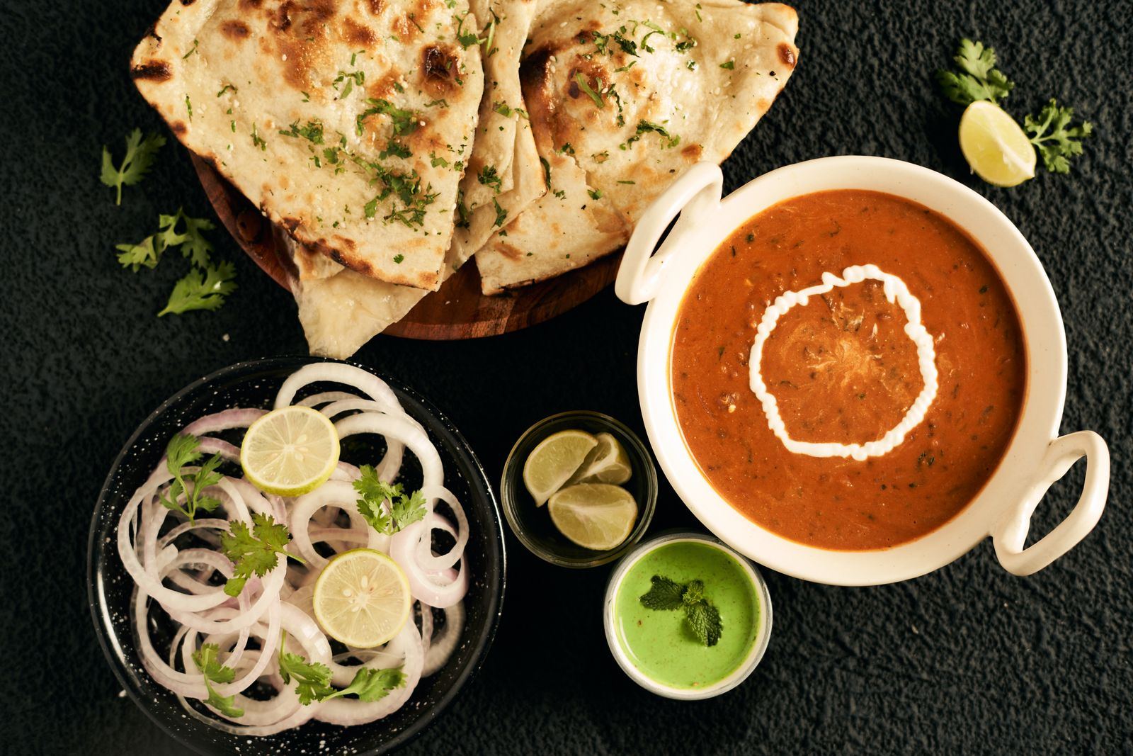 Naan, creamy curry, onion and chutney on a dark table