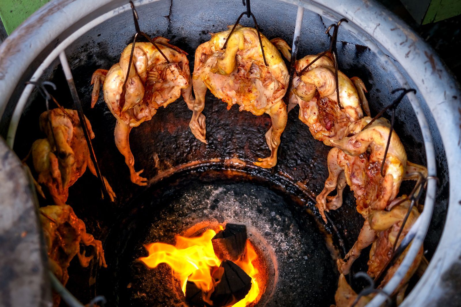 Whole marinated chickens roasting inside a clay tandoor over live flames