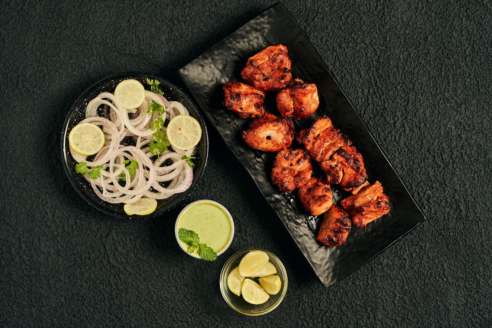 Tandoori chicken pieces with onion and lime on a dark board